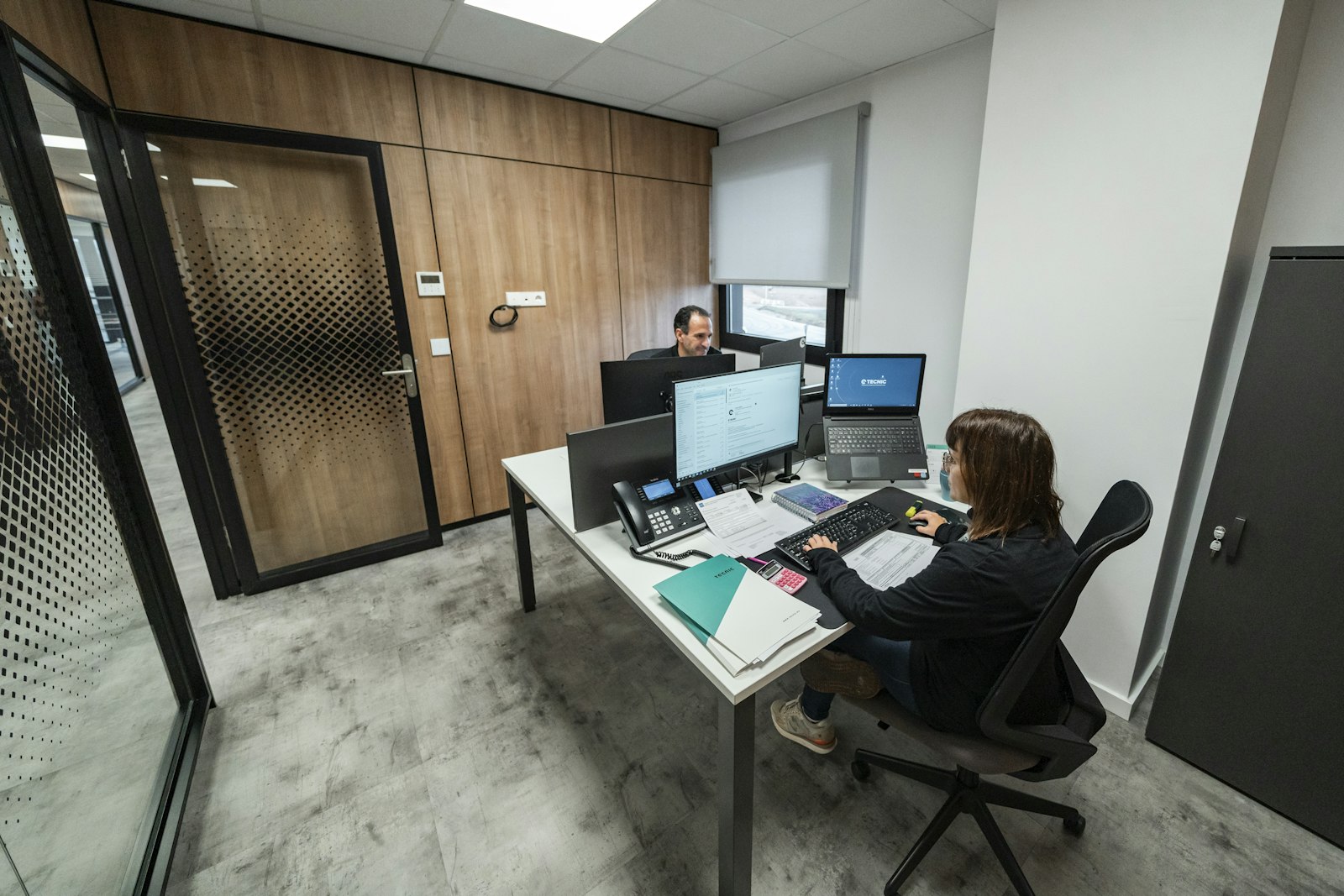 Two colleagues reviewing work together at a desk in a modern office, one explaining something on a laptop screen