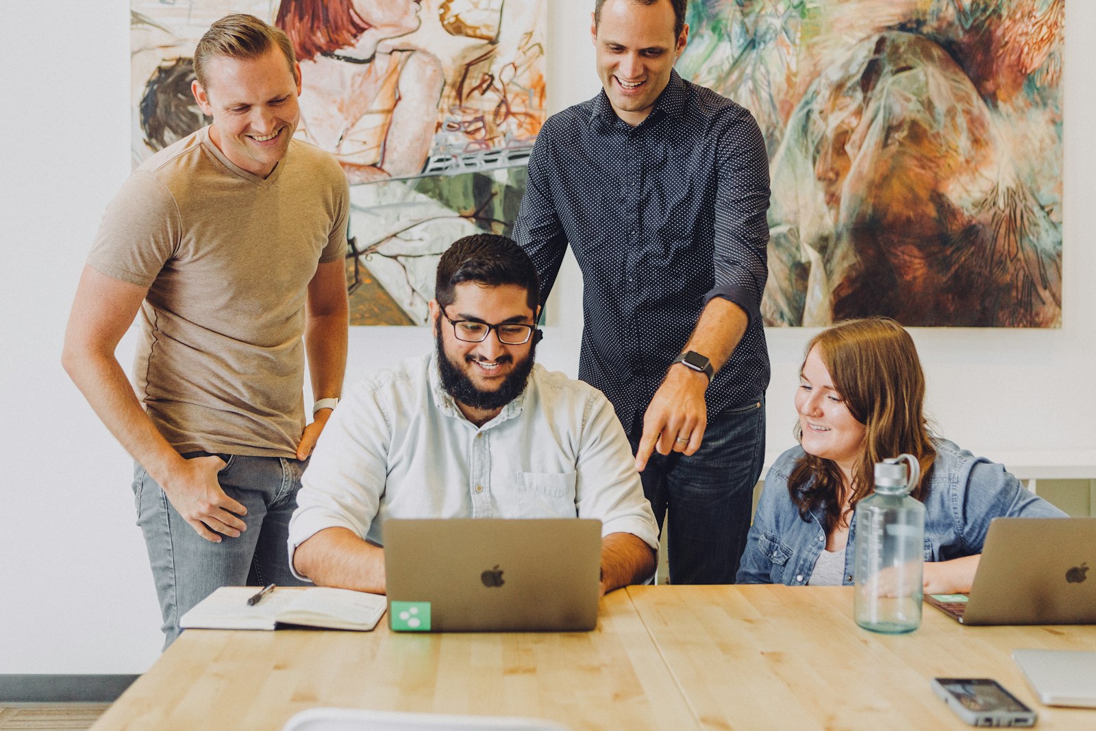 Four coworkers smiling around a laptop while planning a SaaS product launch